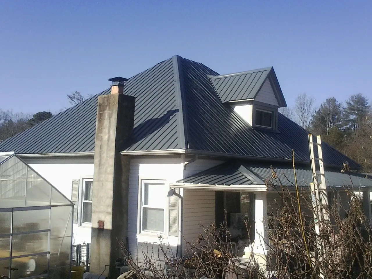 Dark blue standing seam metal roof on a white farmhouse with dormer — Slate & Tile Roof Repair by Roofing Brothers in Reidville