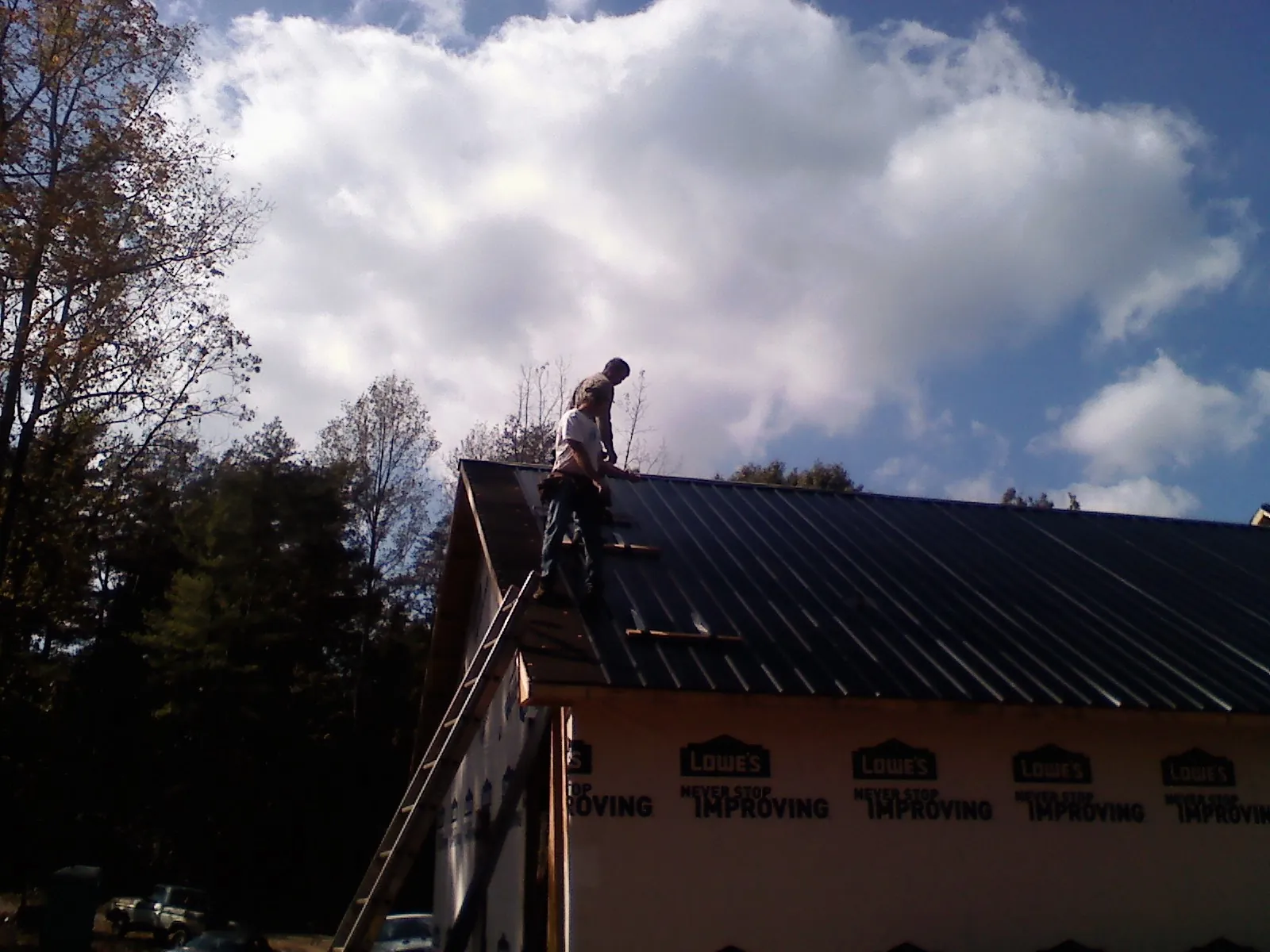 Roofer fastening dark metal panels high against a cloudy sky, from a Roof Inspection job in Reidville