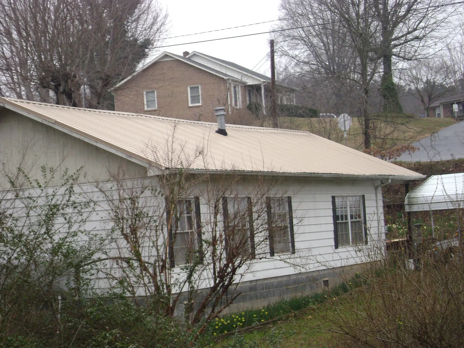 Tan metal roof on a white sided house set into a hillside — Commercial Roofing by Roofing Brothers in Reidville